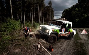 Boomkapper en Boomverzorging Jos Camp die een Boomstam aan het zagen is, en een Witte Land Rover naast hem met het logo van boomkapper.be en in het groot boomkapper.be op de zijkant van de land rover.